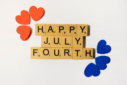 Flat lay of Scrabble tiles spelling 'Happy July Fourth' with colorful hearts, celebrating Independence Day.